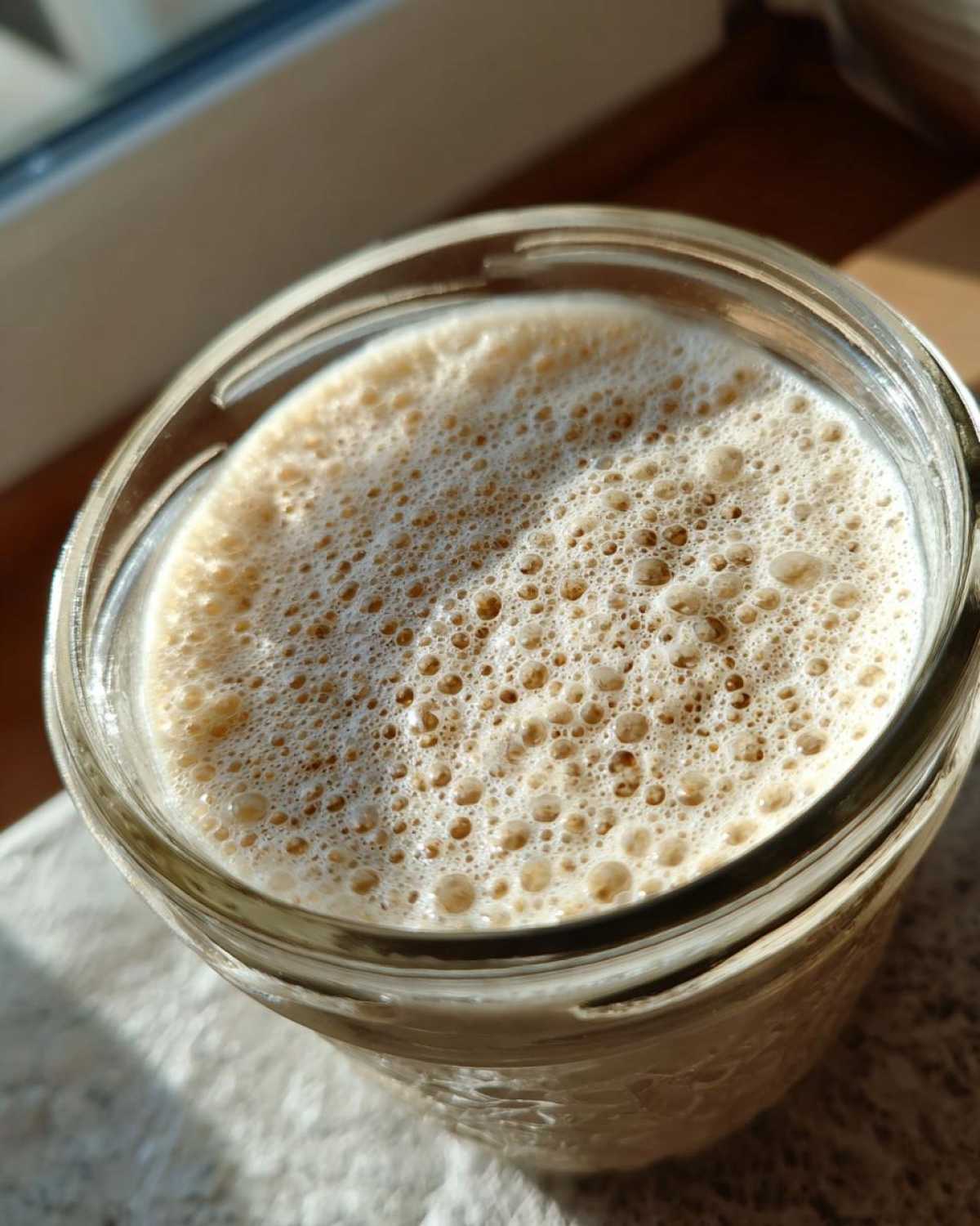 Close-up overhead view of an active sourdough starter with a thick layer of bubbles in a glass jar.