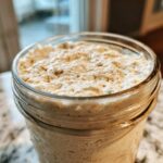 Close-up of an active, bubbly sourdough starter overflowing slightly from the top of a clear glass jar.