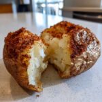 Close-up of a perfectly cooked air fryer baked potato split in half, showing fluffy interior and seasoned crispy skin.
