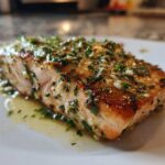 Close-up of a perfectly cooked piece of air fryer salmon topped with a glistening garlic and parsley herb mixture.