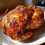 A whole roasted chicken with crispy, seasoned skin, fresh from the air fryer whole chicken preparation.