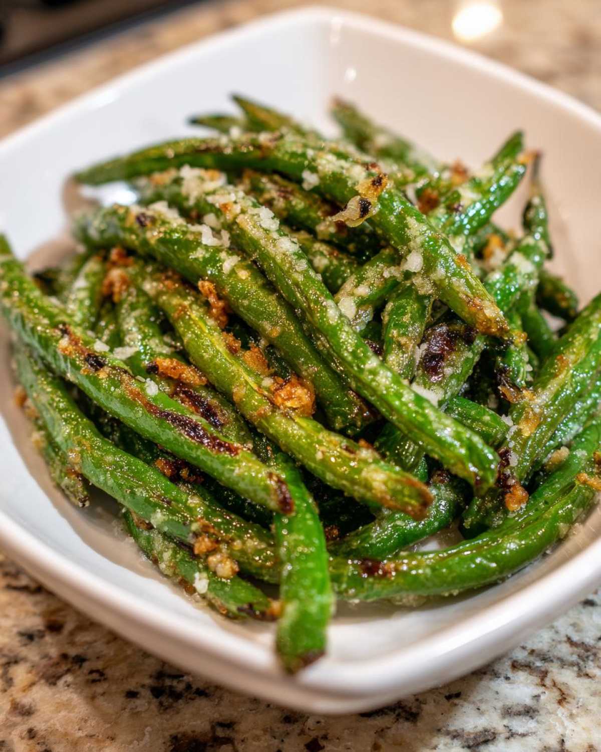 Close-up of roasted green beans topped with grated Parmesan cheese in a white bowl.