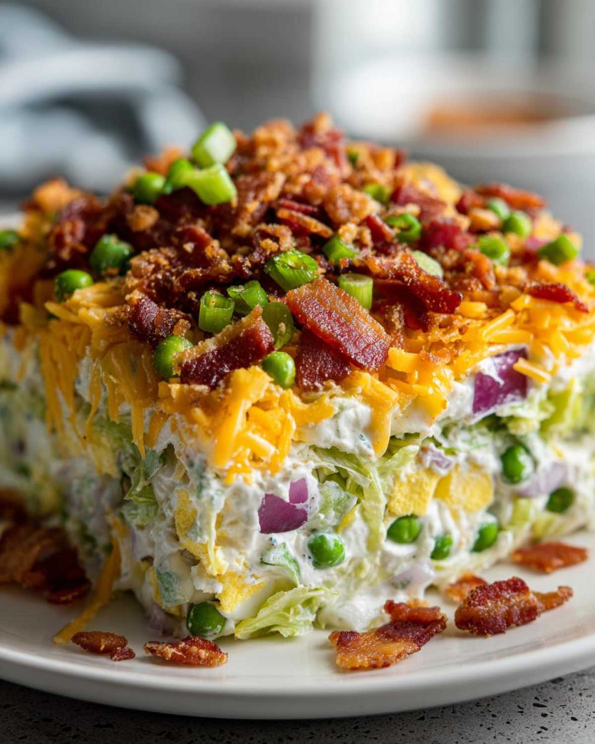 A cross-section view of the amazing 7 layer salad, showing layers of lettuce, creamy dressing, peas, egg, and topped with cheese, bacon, and green onions.