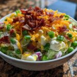 Close-up of the top layer of an amazing 7 layer salad, featuring bacon bits, shredded cheese, and green onions.