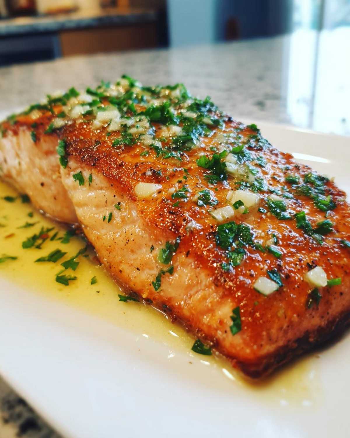 Close-up of a perfectly cooked air fryer salmon fillet topped with melted butter, minced garlic, and fresh parsley.