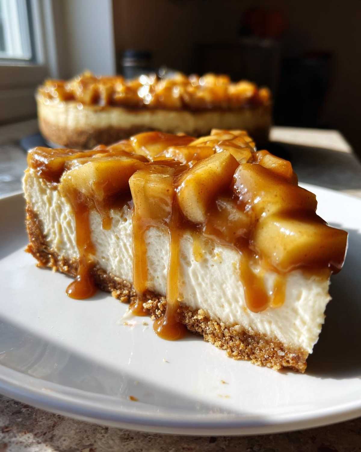 A close-up slice of amazing apple pie cheesecake topped with caramelized apples and dripping caramel sauce.