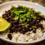 A close-up of a serving of black beans and rice topped with fresh cilantro and a lime wedge.