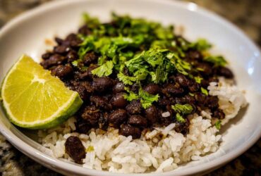 A close-up of a serving of black beans and rice topped with fresh cilantro and a lime wedge.