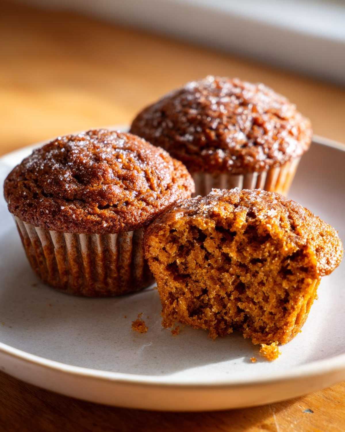 Three delicious bran muffins on a plate, one is broken open showing the moist interior texture.