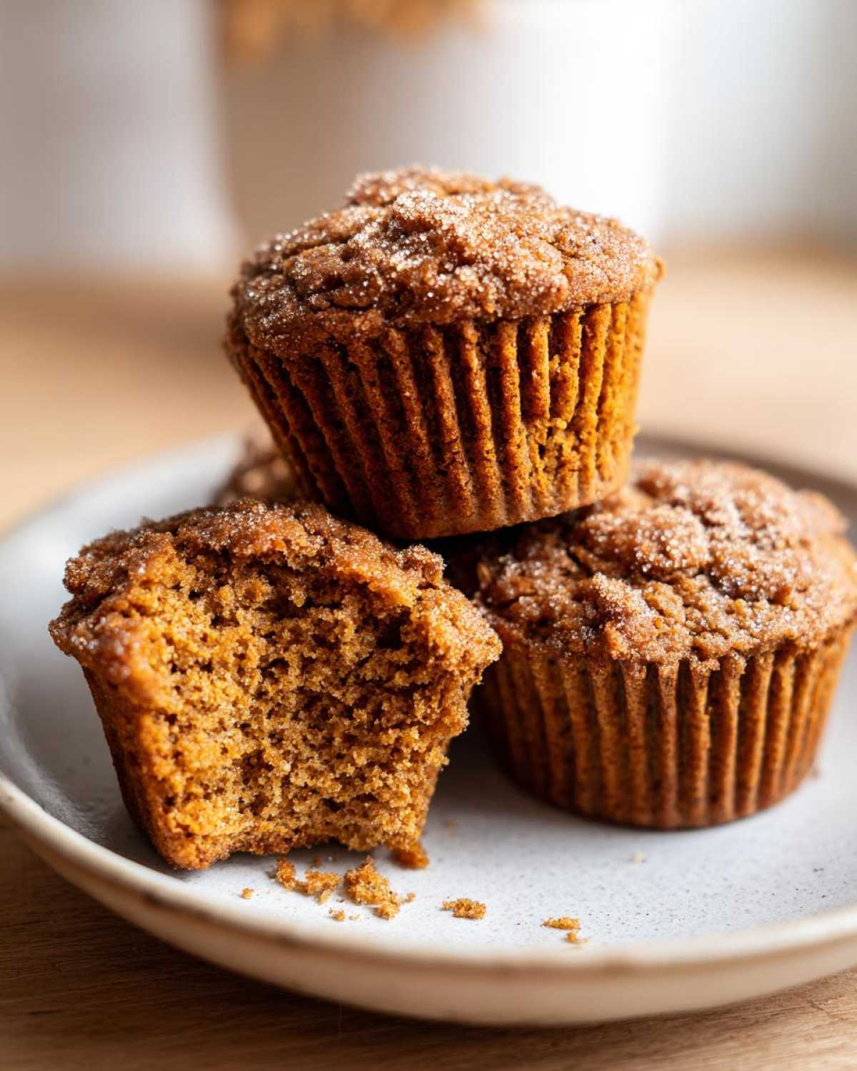 Three moist bran muffins stacked on a plate, one with a bite taken out showing the texture.