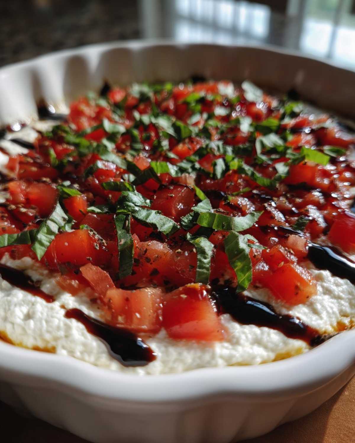 Close-up of a creamy white bruschetta dip topped with diced tomatoes, fresh basil, and a balsamic glaze drizzle.