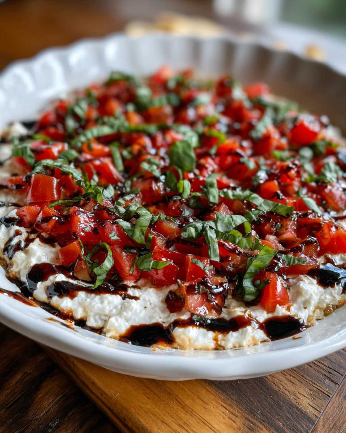 Close-up of a creamy bruschetta dip topped with diced tomatoes, fresh basil, and a balsamic glaze drizzle.