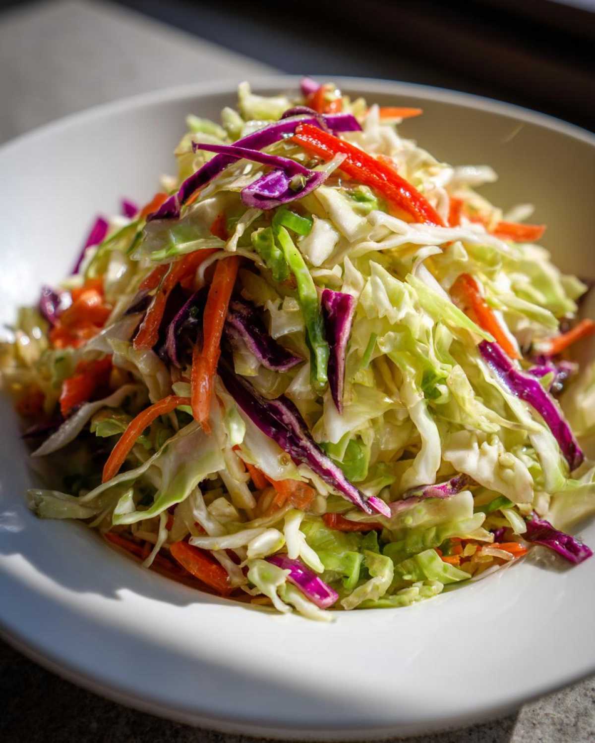 Close-up of a vibrant cabbage salad featuring shredded green cabbage, red cabbage, carrots, and red peppers.