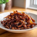 A close-up of a generous serving of deeply browned, glossy caramelized onions on a white plate.