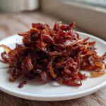 A close-up of a mound of rich, dark brown caramelized onions served on a small white plate.