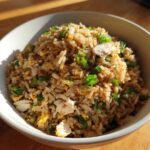 Close-up of a bowl filled with savory chicken fried rice topped with bright green scallions.