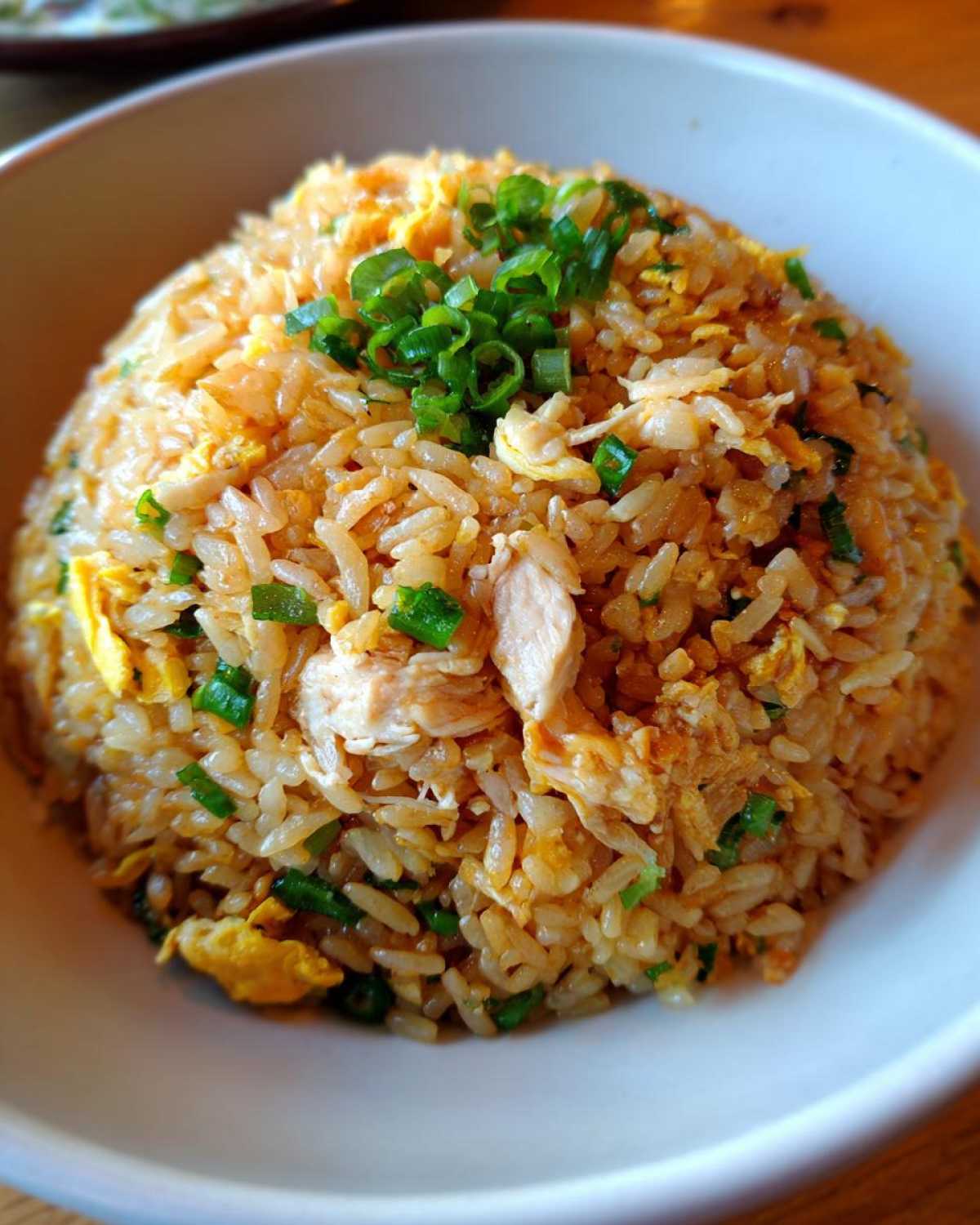 A close-up of a perfectly mounded bowl of amazing chicken fried rice, topped with fresh green onions.