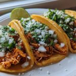 Close-up of three vibrant chicken tacos filled with shredded meat, topped with white onion, cilantro, and cotija cheese.