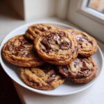 A stack of freshly baked, gooey chocolate chip cookies with melted chocolate chunks on a white plate.