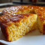 Close-up of a moist slice of cornbread casserole showing corn kernels and a shiny, glazed top.