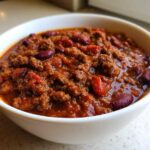 Close-up of a white bowl filled with rich, thick crockpot chili featuring ground meat and kidney beans.
