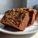 Close-up of two moist slices of date nut bread, rich in raisins and nuts, sitting on a white plate.
