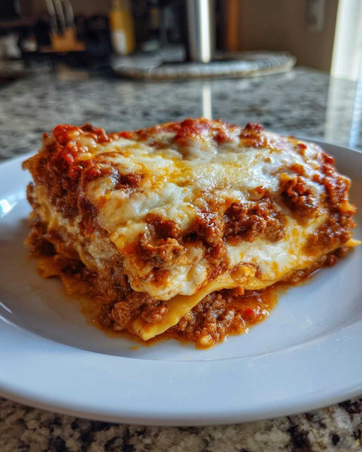 A close-up of a thick, cheesy slice of lasagna with rich meat sauce on a white plate.