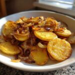 A white bowl filled with perfectly golden brown fried potatoes mixed with caramelized onions.