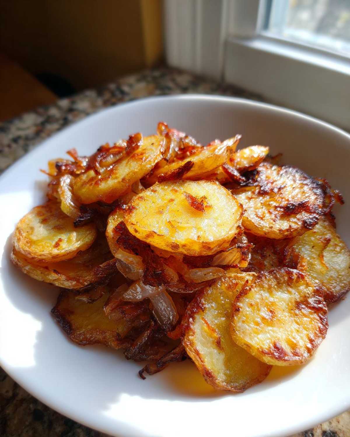 A white bowl filled with perfectly golden brown, crispy fried potatoes and caramelized onions.