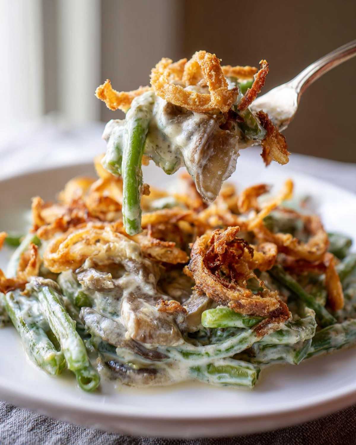 A fork lifts a bite of creamy green bean casserole topped with crispy fried onions.