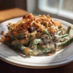 A serving of creamy green bean casserole topped generously with crispy fried onions on a white plate.