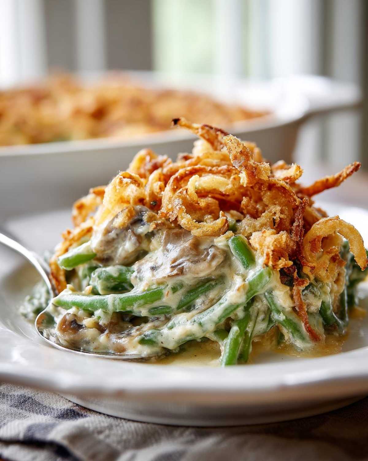 A close-up serving of amazing green bean casserole featuring green beans, creamy sauce, mushrooms, and topped with crispy fried onions.