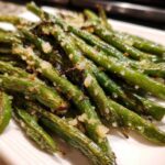 Close-up of perfectly roasted and seasoned green beans piled on a white plate.