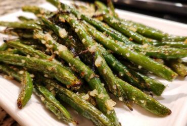 Close-up of perfectly roasted and seasoned green beans piled on a white plate.