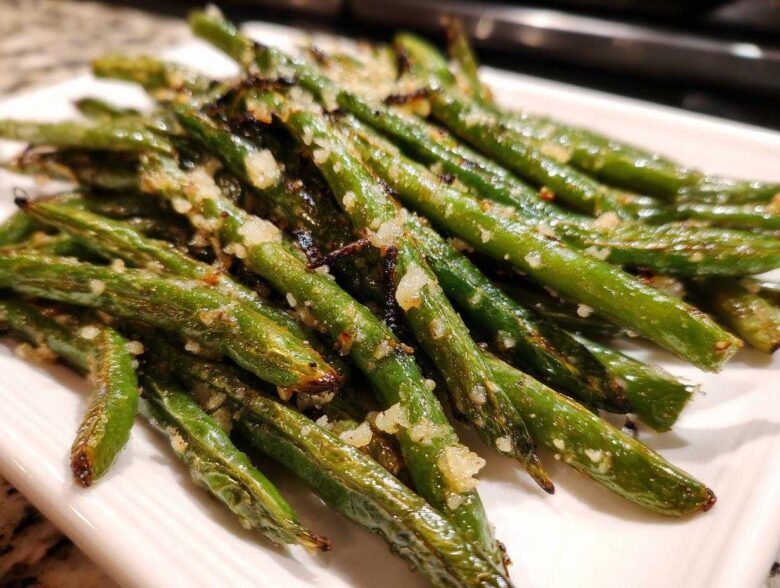 Close-up of perfectly roasted and seasoned green beans piled on a white plate.