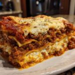 A thick, layered slice of homemade lasagna featuring rich meat sauce, ricotta cheese, and melted mozzarella topping.