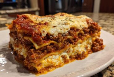 A thick, layered slice of homemade lasagna featuring rich meat sauce, ricotta cheese, and melted mozzarella topping.