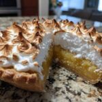 Close-up of a slice removed from a lemon meringue pie showing the thick, bright yellow lemon filling and fluffy, torched meringue.