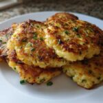 A stack of perfectly golden brown mashed potato cakes, garnished with fresh chives, ready to eat.
