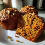 Close-up of a morning glory muffin cut in half showing moist texture, carrots, and walnuts.
