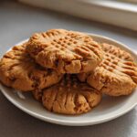 A small stack of freshly baked peanut butter cookies showing classic crisscross fork marks on a white plate.