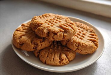 A small stack of freshly baked peanut butter cookies showing classic crisscross fork marks on a white plate.