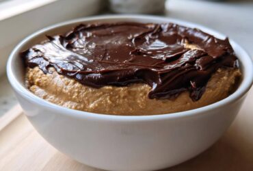 Close-up of a white bowl filled with creamy peanut butter dip topped with a layer of melted chocolate.