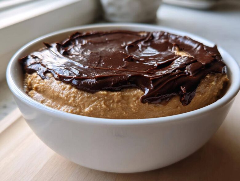 Close-up of a white bowl filled with creamy peanut butter dip topped with a layer of melted chocolate.