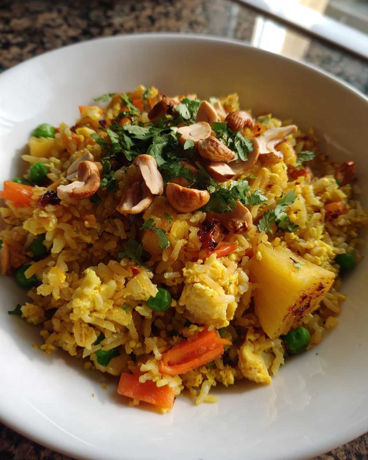 A close-up view of vibrant yellow pineapple fried rice topped with cashews and fresh cilantro in a white bowl.
