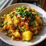 A close-up, tasty serving of pineapple fried rice topped with cashews and fresh cilantro.