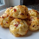 A white plate filled with golden brown, cheesy pizza bites topped with visible bits of bacon or pepperoni.