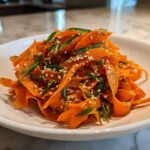 Close-up of a vibrant raw carrot salad made with shaved carrots, green onions, and sesame seeds.
