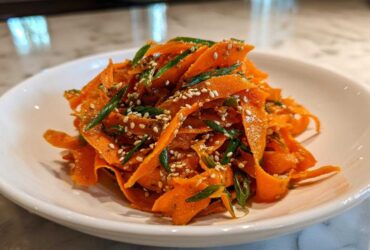 Close-up of a vibrant raw carrot salad made with shaved carrots, green onions, and sesame seeds.
