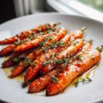 Close-up of glossy, glazed roasted baby carrots topped with fresh thyme sprigs on a white plate.